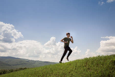 Light-skinned male runner running from grass top of mountain hill. Healthy man joggingの写真素材