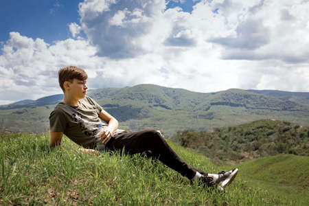 The guy lays on top of the mountain and looks at the landscape. He is holding a bottle of water in...