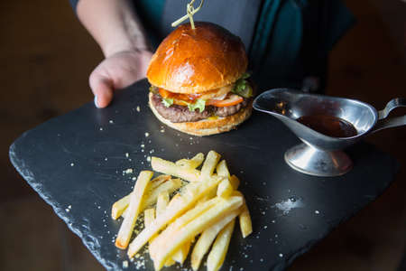 Burger and french fries on a black wooden plateの写真素材