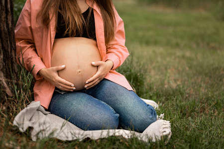Pregnant woman and her husband hugging on the tummy together in nature outdoor