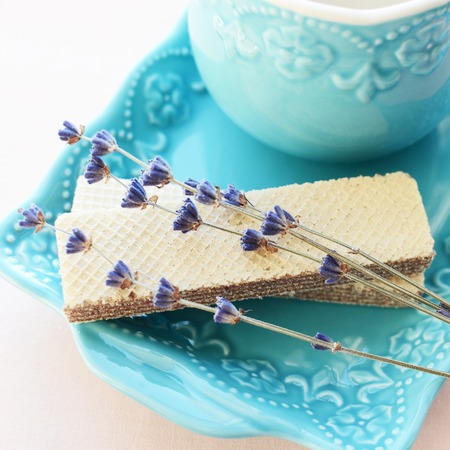 A pair of wafers with lavender flowers and cup of tea on a blue plateの写真素材