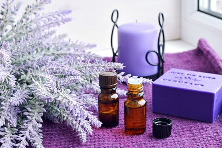 small glass bottles of essential oil, soap and candle with lavender flowers over purple knitted background on window sillの写真素材