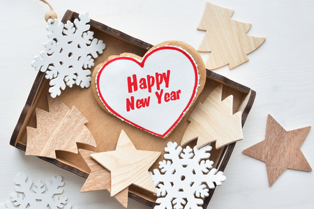 New Year's concept. Heart shaped gingerbread cookies in wooden box, wooden fir-tree, snowflacke and star shapes on wooden white backgroundの写真素材
