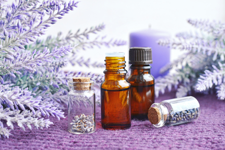 small glass bottles of essential oil, dry lavender flowers with candle over purple knitted backgroundの写真素材
