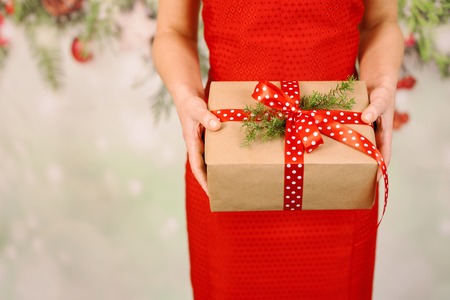 hands of woman in red dress holding christmas gift box tired with satin red ribbonの写真素材