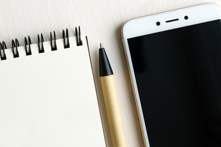 Smartphone, empty notebook and pen over white wooden background, business or study concept mockupの写真素材