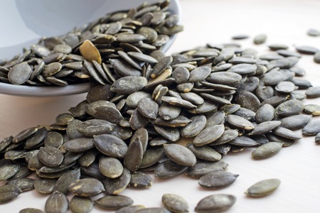 fresh dark green pumpkin seeds scattered from grey ceramic plate over wooden backgroundの写真素材