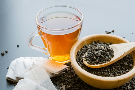 Black tea in a cup, tea bags and dried leaves in wooden bowl with spoonの写真素材