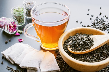 tea in a cup, tea bags, herbs and black tea dried leaves in wooden bowl with spoonの写真素材