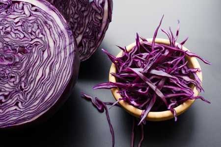 chopped red cabbage salad in wooden bowl with a half of cabbage head over dark gray backgroundの写真素材
