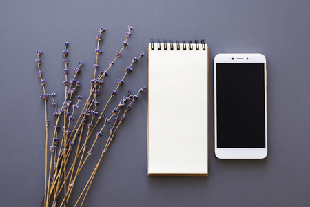 designer working place flatlay with opened notepad, smartphone and lavender dry flowers bunch over purple background, top viewの写真素材