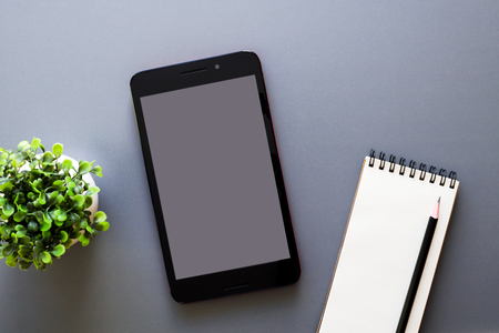 gray background office table workspace with tablet mock up, opened notepad with pencil and green potted plant, top viewの写真素材