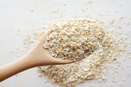uncooked rolled oats in wooden spoon over white backgroundの写真素材