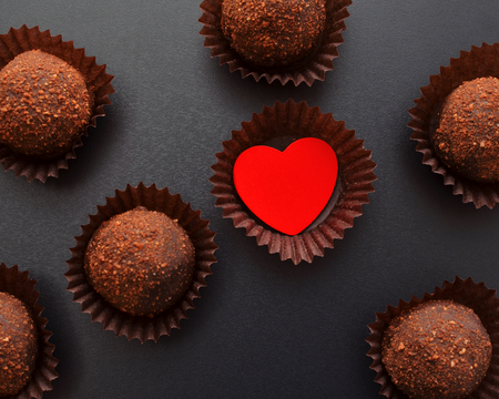chocolate sweets in wrapper with red heart over black background, darkmood photo, top view, Saint Valentines Day cardの写真素材