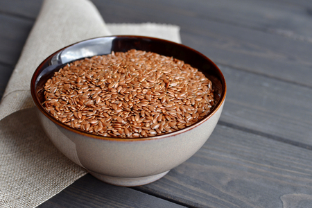 flax seeds in ceramic bowl with linen fabric on dark rustic wooden backgroundの写真素材