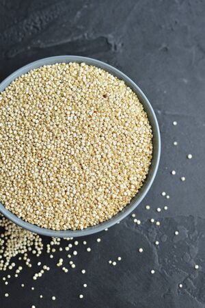 Dry organic quinoa seeds in gray ceramic bowl on dark grunge concrete background, top view, healthy food conceptの写真素材