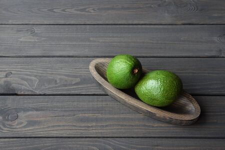 Fresh organic avocado in wooden plate on dark wooden table background, top view