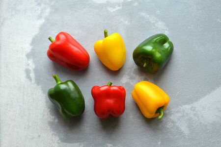 Fresh bell peppers over grey concrete background. Green, red and yellow vegetables. Organic healthy food concept. Top view.の写真素材