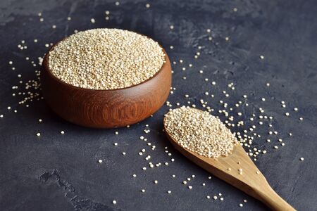 Raw quinoa grains in wooden bowl and spoon on black concrete backgroundの写真素材