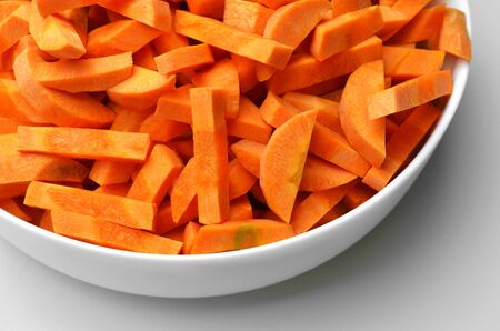 Mediterranean diet. Carrot root chopped in big ceramic bowl on white table background. Vegan food preparation concept.の写真素材