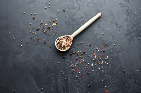 Sea salt, different peppers, cardamon, mustard seeds and red paprika flakes in wooden spoon. Mixture of different kinds of spices on dark grunge background. Top view. Copy space.の写真素材