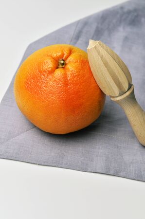Pink grapefruit citrus fruit with wooden hand citrus squeezer on white table background with linen napkinの写真素材