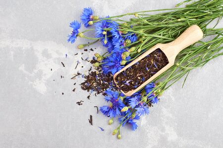 Herbal tea blend flat lay with dried cornflower petals in wooden scoop with fresh cornflowers on grey backgroundの写真素材