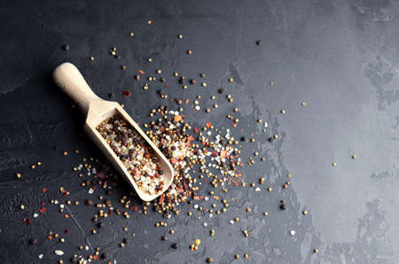 Sea salt, peppers mix, cardamon, mustard seeds and red paprika flakes in wooden scoop. Mixture of different kinds of spices on dark grunge background. Top view. Copy space.の写真素材