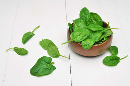 Fresh spinach leaves in wooden bowl over white wooden table. Healthy vegan food. Green living and...