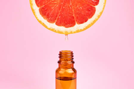 Citrus oil drop dripping from grapefruit slice into dark glass bottleの写真素材