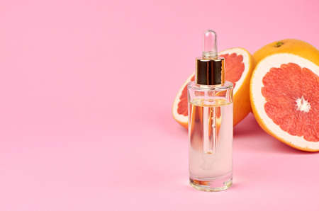 Aromatherapy treatment - citrus essential oil in glass bottle with fresh grapefruit halves on pink background, copy space.の写真素材