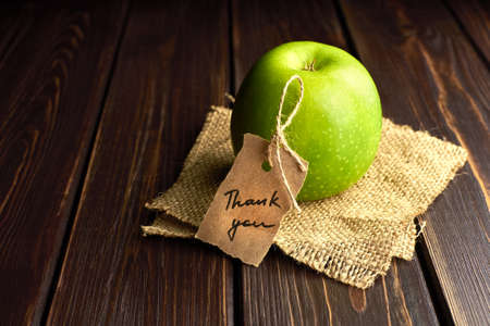Green apple gift with thank you lable on dark wooden table background. Teachers day concept.の写真素材