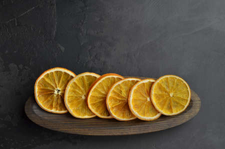 Homemade dried orange chips slices in wooden plate on dark background