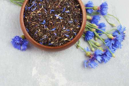 Blend of black tea, dried cornflowers petals and thyme in wooden bowl with fresh blue cornflowers, top viewの写真素材