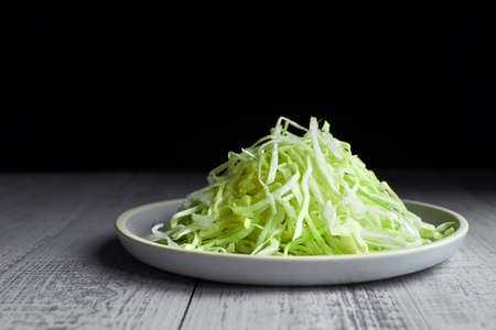 Diet concept. Chopped fresh cabbage salad on white ceramic plate over dark backdrop, copy spaceの写真素材