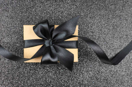 Gift box with black ribbon with a bow on dark glittering background. Black Friday or Fathers Day concept.の写真素材