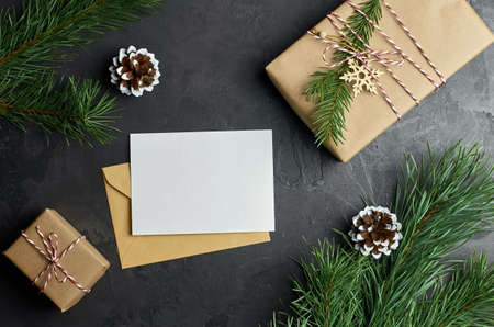 Christmas card mockup with gift boxes and pine tree branches with cones. Christmas composition on dark background. Top view, copy space.の写真素材