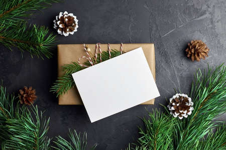 Christmas card mockup with gift box and pine tree branches with cones on dark background. Winter holidays composition, top view, flat lay, copy space.の写真素材