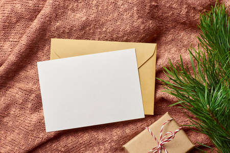 Greeting card mockup with gift box, cones and pine tree branch on knitted background. Christmas flat lay composition with copy space.の写真素材