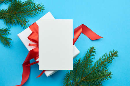 Christmas and New Year greeting card mockup with gift box and fir tree branches on blue paper background, top view, copy space.の写真素材