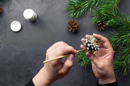 Female hands painting pine cones for christmas decorations over dark background with pine tree branches.の写真素材