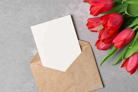 Card or invitation mockup with red tulips bouquet and envelope on grey concrete backgroundの写真素材