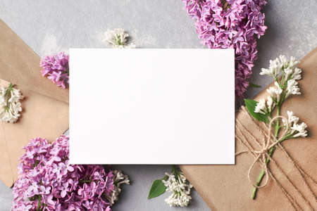 Greeting or invitation card mockup with gift box, envelope and lilac flowers on grey concrete...