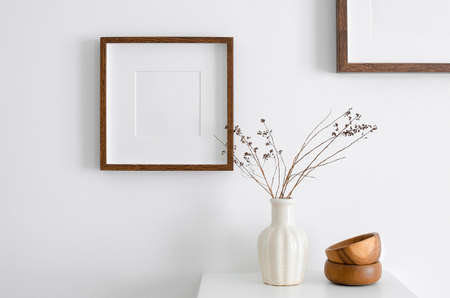 Square wooden frame mockup for artwork, photo, print and painting presentation. White walll with vase, dry twigs and wooden decorations.の写真素材