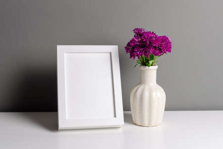 Portrait white frame mockup for artwork, photo and print presentation. Grey walll interior with fresh chrysanthemum flowers in vase.の写真素材