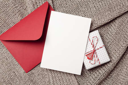 Christmas or New Year greeting card mockup with gift box and red envelope on knitted background