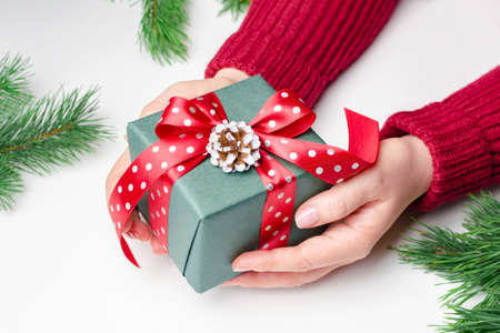 Female hands holding decorated christmas gift box with red bow over white backgroundの写真素材