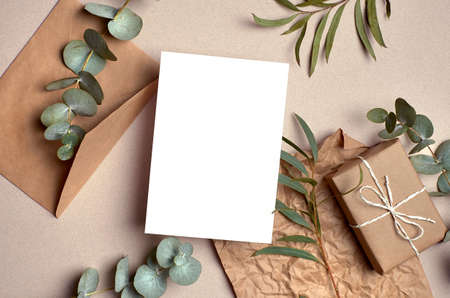 Greeting card mockup with gift box, envelope and natural eucalyptus twigs on paper background. Card mockup with copy space.の写真素材
