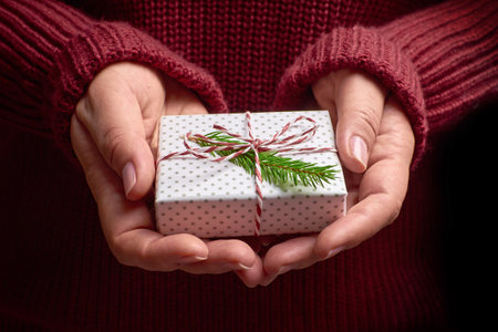 Female hands in cozy sweater holding wrapped christmas gift