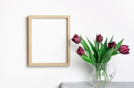Wooden portrait frame mockup with tulips flowers over white wall for artwork presentationの写真素材